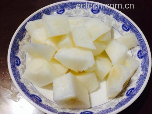 白色瓷盘中摆放着切块的橙黄色脆柿与其他水果混合的水果沙拉,周围点缀薄荷叶,旁边放有一把银色小勺,背景为木质餐桌 脆柿水果沙拉摆盘