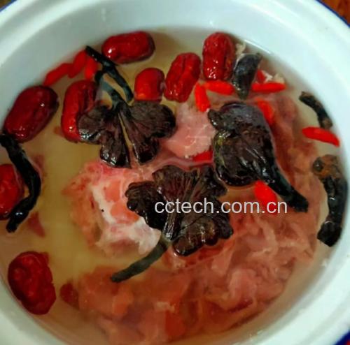 一杯冲泡好的竹灵芝水置于白色瓷杯中,液体呈清澈金黄色,杯口微微冒着热气,旁边配有竹制托盘、新鲜枸杞数粒和一本打开的养生笔记,营造出自然健康的饮用氛围 竹灵芝成品饮品展示