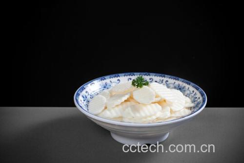 一位家庭主妇正在白色瓷碗中用透明液体浸泡切好的藕片,旁边摆放柠檬、玻璃量杯、不锈钢夹子,台面整洁,体现科学处理食材的过程 家庭厨房中处理藕片的操作场景
