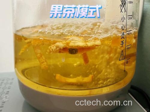 一只透明玻璃锅置于电磁炉上,锅中有清水正在沸腾,水中漂浮着数块浅棕色的罗汉果碎片,蒸汽袅袅上升,旁边放置一个陶瓷杯,杯中已倒入金黄色的罗汉果茶汤,背景为厨房操作台,左侧摆放一整颗未拆封的干罗汉果 罗汉果煮水过程图
