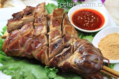 一整盘刚出炉的烤羊白条摆放在木质托盘中,肉块油亮红润,边缘微焦,撒有新鲜孜然和葱花点缀,旁边配有一碟辣椒干料和一小碗蒜泥醋汁,背景虚化的餐桌上还有馕饼和啤酒 烤羊白条成品摆盘图