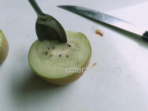 一张白色背景下的组合图片:左侧是一个完整的成熟黄心猕猴桃,表皮棕褐色带细绒毛;右侧是同一品种横向切开的果实,展示出鲜明的金黄色果肉和放射状黑色种子排列,果肉湿润有光泽,旁边放置一把不锈钢勺子,暗示可直接挖食 成熟黄心猕猴桃与剖开对比图
