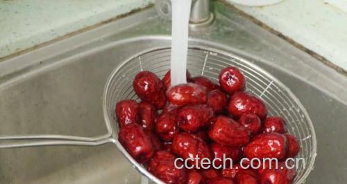 一位厨师正在用流动清水冲洗置于不锈钢滤网中的干红枣片,背景为整洁厨房台面,光线明亮自然,突出食材清洁过程 红枣片清洗过程