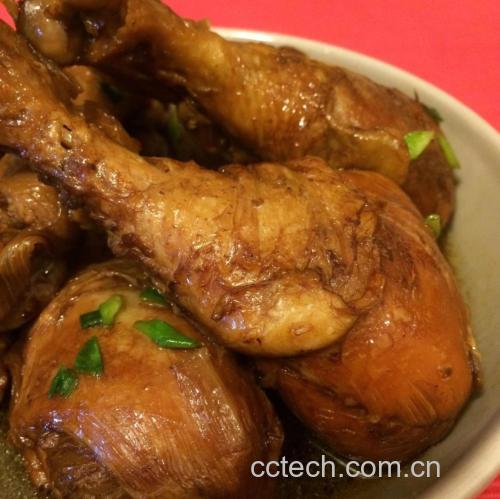 一口黑色铸铁锅中正炖煮着金黄色的鸡腿块,汤汁微微冒泡,周围可见大葱段和姜片,蒸汽袅袅上升,背景为暖色调厨房环境,突出食物的温暖氛围 大葱炖鸡腿正在炖煮过程