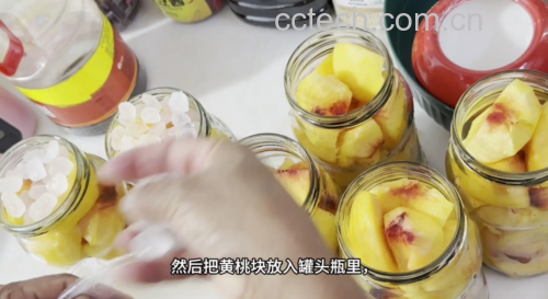 厨房台面上摆放着玻璃罐装的新鲜黄桃块、一瓶打开的原味酸奶、一个搅拌碗和一把不锈钢勺,正在将黄桃倒入酸奶中进行混合,展示家庭自制黄桃酸奶的过程,强调食材透明与手工制作的安全感 黄桃酸奶制作过程示意图