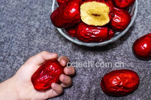 一碗正在熬制的红枣小米粥,锅中漂浮着数颗裂口的骏枣,旁边摆放着整颗骏枣和去核骏枣,展示其在日常饮食中的多种用途 骏枣烹饪应用