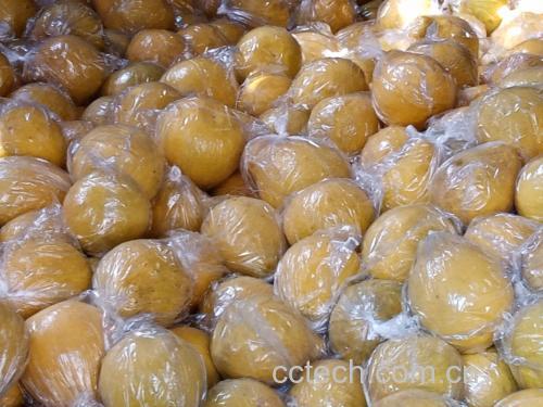 一位消费者正在超市水果区用手掂量两个沙田柚的重量,并用另一只手轻敲其中一个果体,旁边摆放着标签注明‘广西容县特级沙田柚’的纸箱 沙田柚手感与敲击检测场景图
