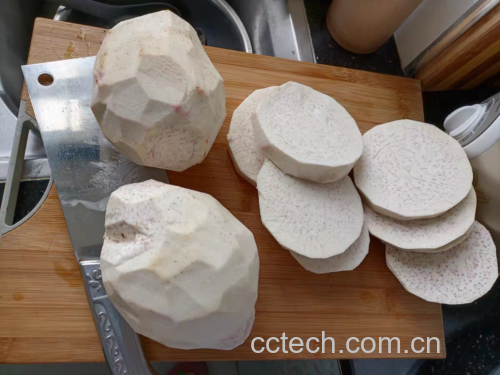 一位厨师戴着乳胶手套正在砧板上用削皮刀处理新鲜荔浦芋头,芋头已去皮并切成均匀的立方体小块,旁边放置一碗清水用于浸泡,背景为整洁厨房台面 荔浦芋头去皮切块过程特写