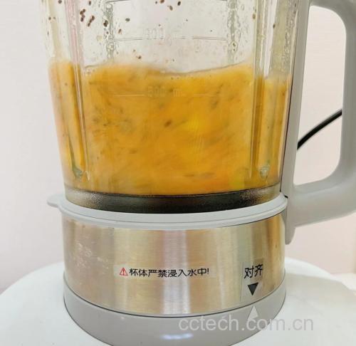 料理机中正在搅打黄桃与牛奶混合物,液体呈淡黄色乳状,机器透明杯体清晰可见内部旋转状态,背景为现代厨房环境 图片描述