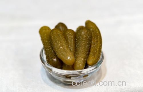 一碗透明玻璃碗中盛放着由小黄瓜薄片、原味酸奶和少许薄荷叶组成的冷食沙拉,旁边摆放一把小勺,背景为木质餐桌与暖色调灯光,营造出晚间放松用餐氛围 小黄瓜与酸奶混合沙拉