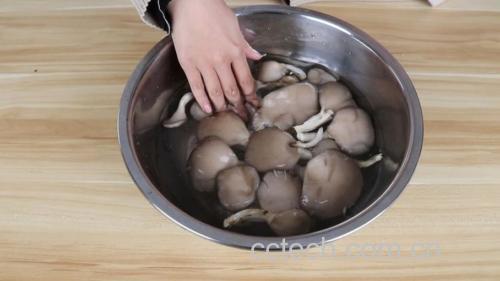 一位厨师正在操作台上将新鲜平菇用手撕成细条,旁边摆放着一碗淡盐水和厨房纸巾,展示平菇清洗与初步处理的过程 平菇清洗与撕条过程