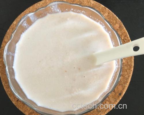 特写镜头显示一只手持筷子在白色瓷碗中搅拌面糊,碗内为乳白色略带颗粒感的液体,旁边摆放着量勺、面粉、淀粉和鸡蛋,清晰展示调糊配料与状态 调制炸平菇面糊的过程