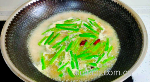 一位家庭主妇在厨房用铁锅清炒四季豆,锅中菜肴色泽翠绿,配有蒜片和红椒丝,灶台整洁,光线明亮,展现健康家常烹饪场景 家庭烹饪四季豆