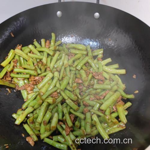 一口铁锅中正在干煸白不老豆角,豆角表面微皱泛黄,旁边有蒜末、干辣椒和肉末混合翻炒,锅气十足,背景为厨房灶台,展现烹饪过程的动态场景 图片描述