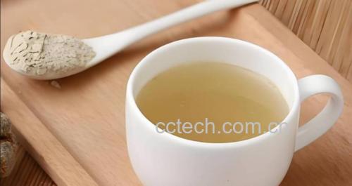 一个干净的厨房台面上,一只透明玻璃杯盛有刚冲调好的三七粉饮品,液体呈淡黄褐色,轻微悬浮;旁边放有一只陶瓷小碗装着浅黄色细腻粉末状三七粉,还有一颗完整的灰黄色三七根,背景虚化,突出天然食材的日常应用场景 三七粉冲泡饮用示意图:透明玻璃杯中加入淡黄色三七粉,倒入温水搅拌,旁边放置一勺三七粉和整颗干燥三七