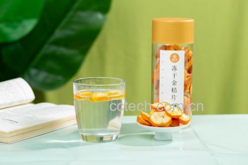 厨房场景中,一只手正在将切好的金桔片放入玻璃罐中,旁边摆放蜂蜜瓶、干净勺子和标签纸,背景为木质操作台和绿色植物,体现健康自然的生活方式,强调家庭自制的安全与营养保留 家庭制作金桔蜂蜜饮品过程图