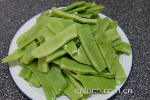 一锅沸水中正在焯烫绿色扁豆,水面漂浮着少量气泡,旁边摆放着洗净切好的扁豆段,厨房台面上有盐罐和油瓶,体现加盐加油的细节 扁豆焯水过程