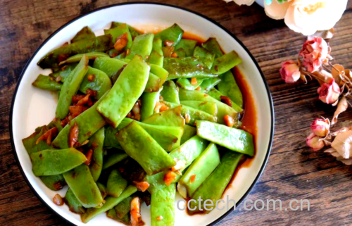 一盘刚出锅的新鲜红扁豆炒菜,豆荚呈亮红色,略带油光,搭配黄色胡萝卜丁和绿色蒜苗段,盛放在白色瓷盘中,背景虚化,体现家常菜肴的真实质感 新鲜红扁豆烹饪成品图