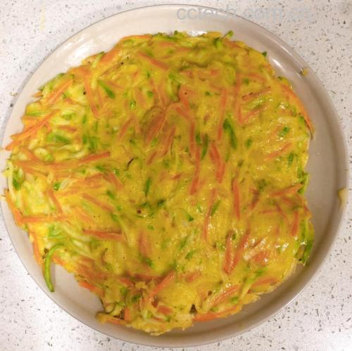 一张金黄色的红皮萝卜丝煎饼,表面酥脆微焦,能看到嵌入的粉红色萝卜丝和绿色葱花,切成三角形摆放在木质砧板上,背景为厨房环境,旁边有一碟酱油蘸料 红皮萝卜丝煎饼特写