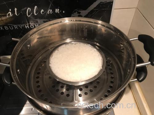 一口不锈钢锅中正在煮着几根带叶的糯玉米,水面微微沸腾,蒸汽袅袅升起,显示中小火状态,旁边放着计时器和调味料瓶 糯玉米在锅中用中小火慢煮的过程