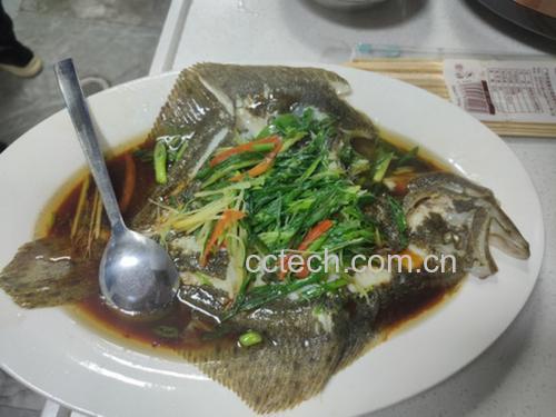 一口不锈钢蒸锅正在冒热气,锅盖微开,里面清晰可见一条完整的清蒸多宝鱼,鱼身上铺着姜片和葱段,盘底有少量汤汁 图片描述