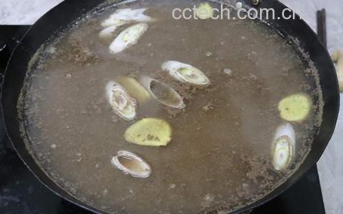 一口黑色铸铁锅中正炖煮着金黄色的豆腐块和乳白色的大葱段,汤汁微微收浓,蒸汽升腾,旁边摆放着生抽瓶和葱段原料,展现烹饪过程 铁杆大葱与豆腐同锅炖烧的场景