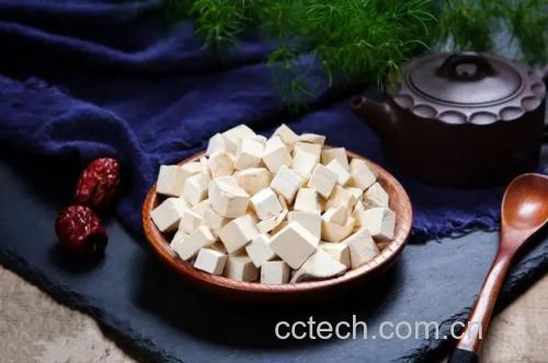 桌面上摆放着四味中药材:左侧为灰黄色的白术片,断面有油点;上方为白色球状茯苓块;右下方为橙红色陈皮丝;左下方为黄褐色党参段。背景为中医养生茶包制作场景,配有研磨钵和陶瓷煎药壶 白术片与其他常见健脾药材组合图