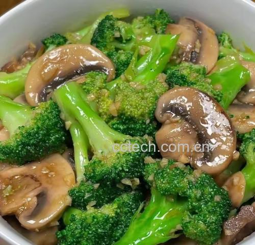 不锈钢炒锅中正在翻炒的绿色西兰花小朵与白色蘑菇片混合,伴有蒜瓣和少许红色辣椒,油光适度,呈现健康家常菜烹饪场景 西兰花与蘑菇清炒过程中的锅具特写