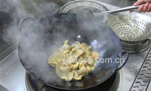 一位厨师正在厨房中用铁锅翻炒切片的新鲜牛肝菌,锅中冒出蒸汽,旁边摆放着葱姜蒜调料,灶台整洁,体现安全烹饪场景 野生菌烹饪过程图