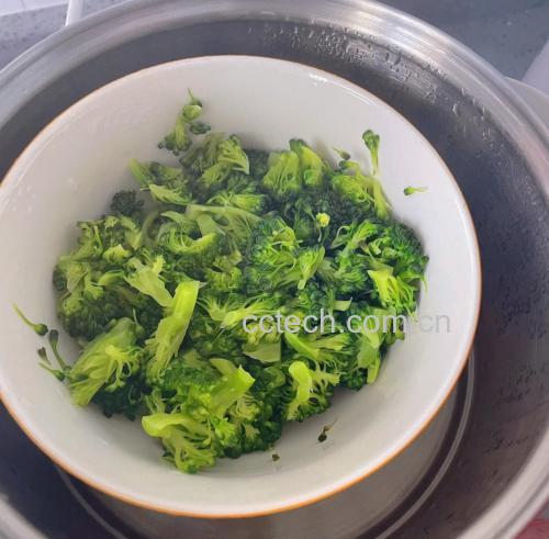 俯拍高清图:纯白瓷盘中盛放刚蒸好的西兰花,花球翠绿如翡翠、边缘微透光,表面无水渍,散落金黄蒜末、雪白芝麻与细碎柠檬皮屑,背景虚化显示不锈钢蒸锅与计时器定格在7:00 蒸制完成的西兰花摆盘图