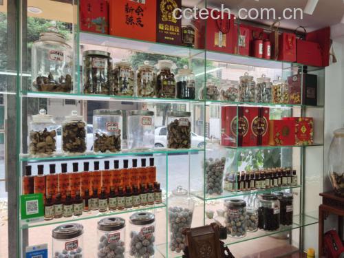 市场实景照片:木质柜台陈列多个布袋,分别标有‘新会陈皮’‘川麦冬’‘有机生姜’字样;一位摊主正在称量陈皮,背景可见中药柜和放大镜,突出专业氛围 中药材市场摊位实景图