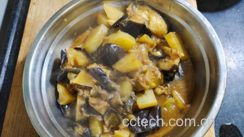 一碗刚出锅的排骨土豆茄子炖菜特写,红褐色汤汁浓郁光亮,排骨色泽油润,土豆块分明,茄子条软糯,表面撒有绿色葱花,旁边配有一碗白米饭,整体构图突出食物的食欲感与家庭温馨氛围 图片描述