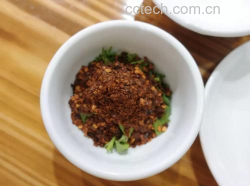 一双戴着食品级手套的手正在一个透明玻璃碗中轻轻翻拌切段的香菜,碗中可见蒜片、小米辣、花椒粒等配料,香菜色泽翠绿,调料分布均匀 腌制香菜拌料