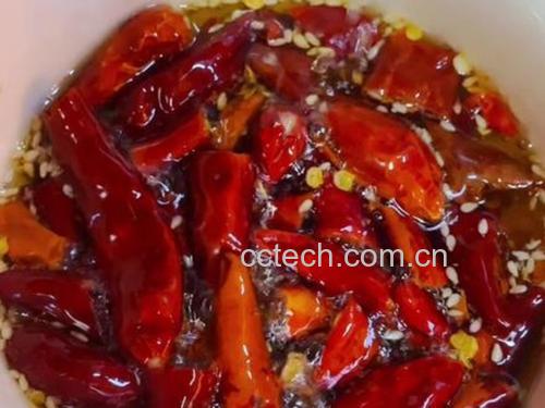 一名穿着围裙的厨师站在厨房操作台前,左手扶着瓷碗,右手持勺将金黄色热油缓缓倒入盛有红辣椒碎和白芝麻的容器中,油面泛起细密气泡,蒸汽袅袅上升 厨师正在将热油缓缓倒入装有辣椒碎和芝麻的陶瓷碗中,油花翻滚,香气四溢