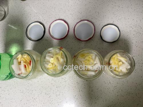 透明玻璃腌菜罐中分层码放着绿色鲜辣椒,中间夹杂白色蒜片和姜片,花椒零星点缀,液体刚没过食材,手正拧紧玻璃旋盖,展示家庭手工腌制细节 腌制过程装瓶图