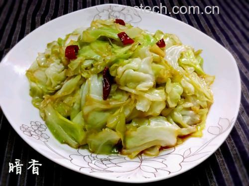 一盘色泽红亮、点缀白芝麻的麻辣白菜摆放在白色瓷盘中,周围有筷子夹起一角,展示其脆嫩条状结构,背景为木质餐桌,氛围温馨 成品麻辣白菜装盘效果