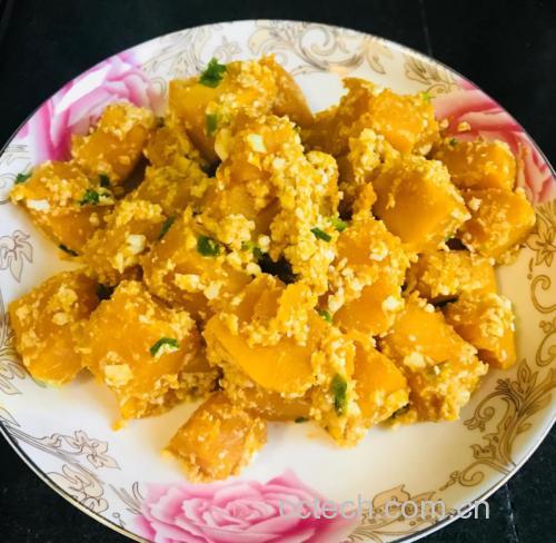 一盘色泽金黄诱人的咸蛋黄炒南瓜,南瓜片裹满细腻泡沫状的咸蛋黄酱,边缘微焦,盛放在白色瓷盘中,背景为中式厨房灶台 咸蛋黄炒南瓜成品图