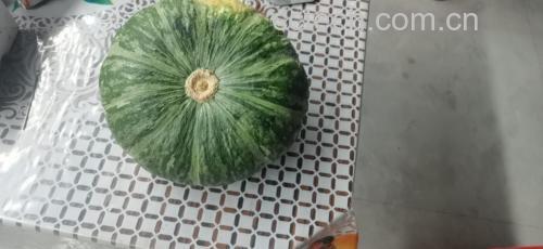 一个完整的板栗南瓜放置在木质砧板上,表皮呈均匀的橙黄色,略带浅绿色条纹,顶部带有绿色瓜蒂,光线柔和,背景为厨房环境 板栗南瓜整体外观特写