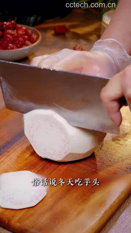 一位厨师正在厨房案板上佩戴乳胶手套削毛芋头,旁边有切好的芋头条,锅中正在蒸煮芋头,蒸汽升腾,场景整洁明亮 厨房中处理毛芋头的过程