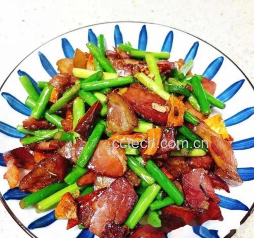 厨房场景中,厨师正在用铁锅爆香蒜片,锅中红菜苔翻炒,色泽鲜亮,蒸汽升腾,旁边摆放已处理好的红菜苔段、蒜瓣、腊肉片等配料,展现家庭烹饪真实情境 红菜苔家常炒制过程