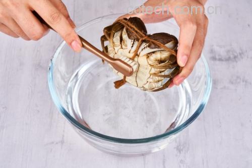 一位厨师戴着手套,正在用软毛刷仔细刷洗一只青壳大闸蟹的背部、腿部和腹部,水槽中有流动的清水,背景为厨房操作台,光线明亮清晰 清洗大闸蟹的过程