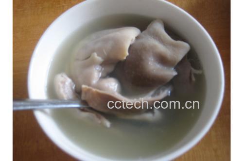 一碗热气腾腾的乳白色猪肚汤,碗中可见清晰的猪肚条、胡萝卜块和玉米段,表面漂浮着细小油珠和葱花,背景为木质餐桌,氛围温馨 白胡椒猪肚汤成品盛碗特写