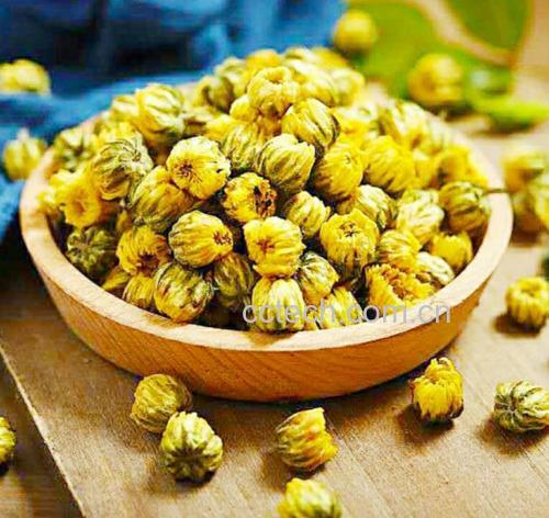干燥的杭白菊花朵,花瓣洁白紧密,花心淡黄,呈球形簇状,背景为浅色木质桌面,旁边配有玻璃茶杯和散落的几朵干花,展现其作为养生茶饮原料的形态 杭白菊干花特写
