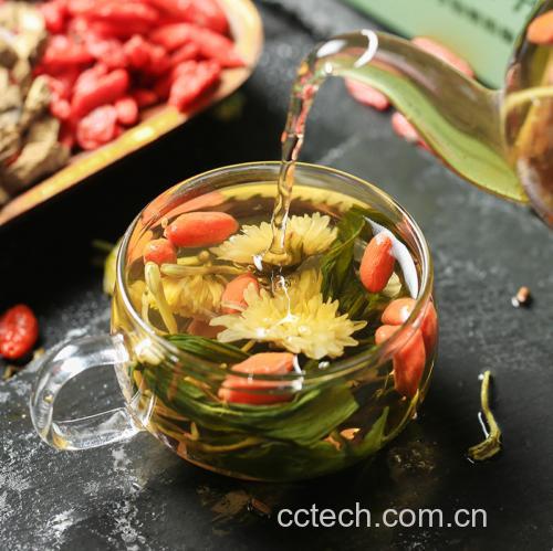 玻璃杯中正在冲泡野菊花茶,热水倒入后花朵缓缓舒展,水中呈现淡黄色澄清液体,几朵完整的野菊花漂浮于水面,背景为厨房台面,旁边放置陶瓷茶罐和量勺,体现家庭养生场景 野菊花茶冲泡过程