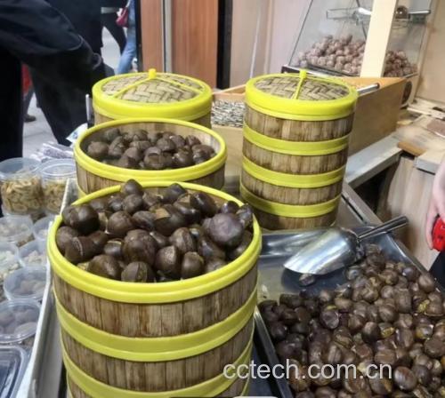 一位师傅正在手工包制板栗酥,案板上摆放着金黄色的板栗泥团和圆形酥皮,手中正在将馅料包裹入皮中,背景为传统烘焙坊工作台,墙上挂着“迁西板栗专用”标识牌 手工制作板栗酥过程