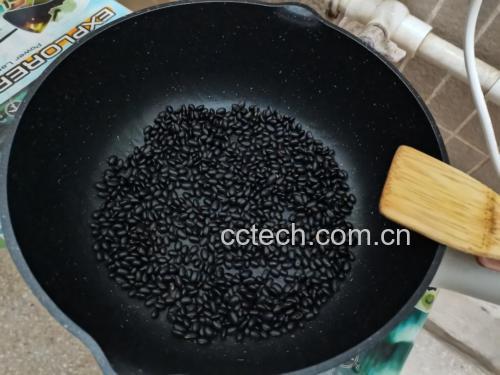 一位厨师正用木铲在传统铁锅中翻炒黑豆,锅内黑豆呈深黑色,表面微微开裂,散发热气,灶台为中式柴火风格,背景可见调料瓶和干豆原料 干黑豆在铁锅中被手工翻炒的场景