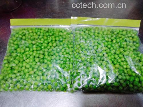 一口不锈钢锅中沸水翻滚,正在焯烫青豌豆;旁边玻璃碗盛有冰水,另一托盘上铺满晾干的绿色豆粒;右侧手部正将豆粒装入透明密封袋,背景可见冰箱冷冻室门半开 青豌豆焯水与冷冻分装