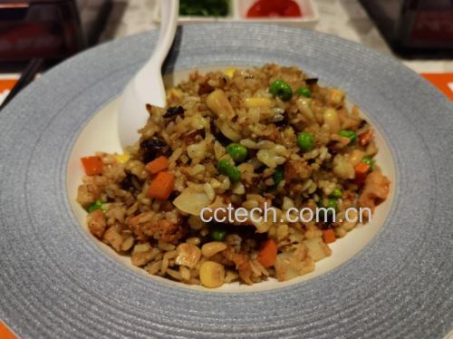一个白色餐盘中盛放着由胡萝卜丁、玉米粒和青豌豆组成的彩色蔬菜炒饭,豆粒饱满翠绿;旁边摆放木铲和玻璃调味瓶,背景为现代厨房灶台,暖光照明 冷冻青豌豆烹饪应用场景
