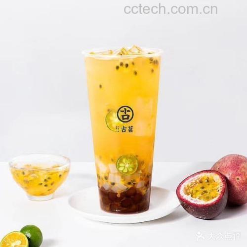 一杯冰镇金桔百香果茶特写,杯身凝结水珠,搭配柠檬片与薄荷叶,呈现清凉夏日饮品氛围 玻璃杯中盛放冰镇金桔百香果茶,杯壁有水珠,杯口插着柠檬片和薄荷叶,背景为夏日阳台绿植