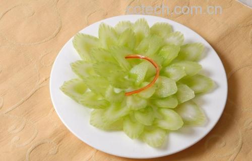 一碗用焯水后的山芹菜叶制作的凉拌菜,配以红椒丝、蒜粒和白芝麻点缀,色泽翠绿诱人,摆盘精致,背景为木质餐桌和竹制餐具,体现自然健康的饮食风格 山芹菜叶料理成品图